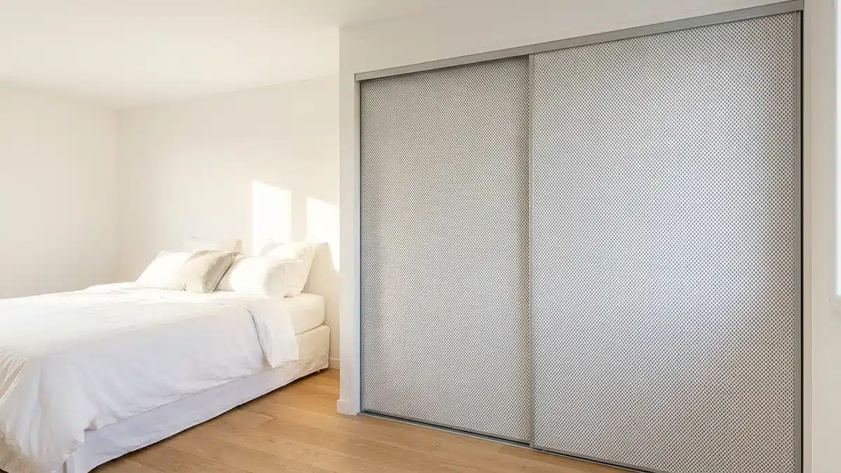 Chambre lumineuse avec un placard à deux portes coulissantes habillées d'un papier peint à petit motif géométrique gris, coupé net au bord de chaque porte